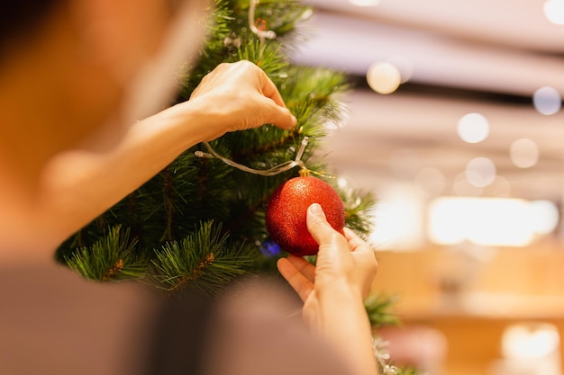 Woman's hand hang a Christmas ball on Christmas tree holiday festive