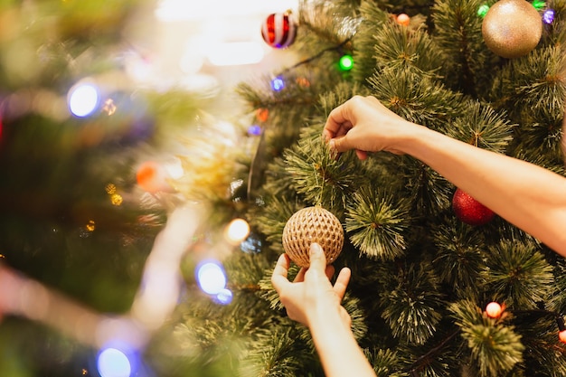 Woman's hand hang a Christmas ball on Christmas tree holiday festive