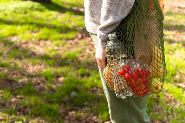 Woman's hand hold a green eco cotton string bag with organic food.