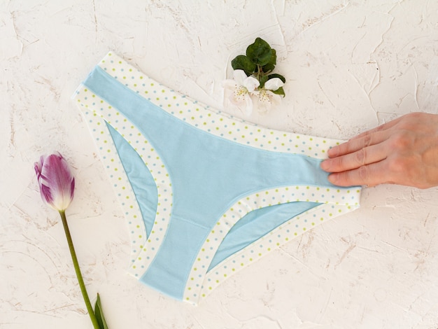 woman's hand holding beautiful blue cotton panties on the white structured background