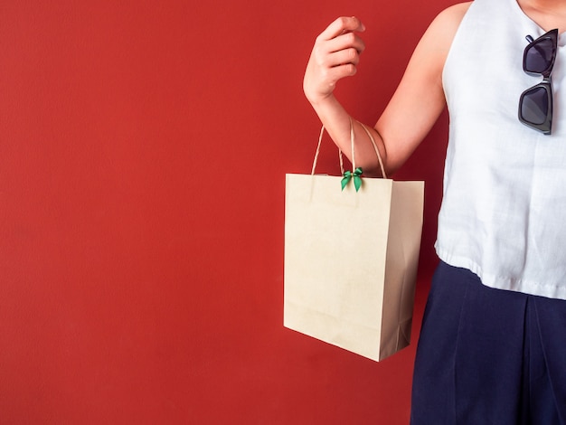 Woman's hand holding blank recycled paper bag decorate with green bow on red wall