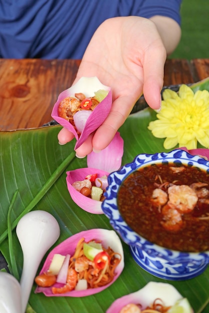 Woman's Hand Holding Fresh Lotus Petal Wrapped Appetizer before Putting Spicy Dip