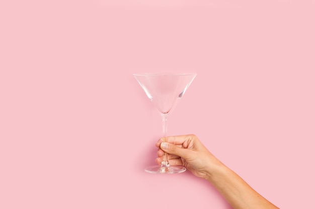 A woman's hand holding a martini glass against a pink background