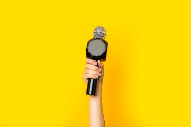 Woman's hand holding a microphone on a bright yellow background