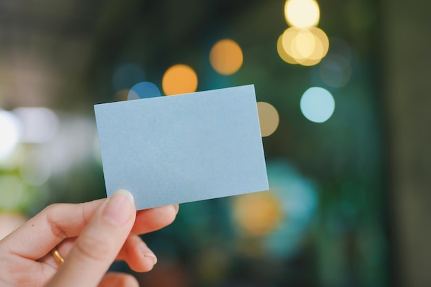 Woman's hand holding a small blank blue paper with bokeh background