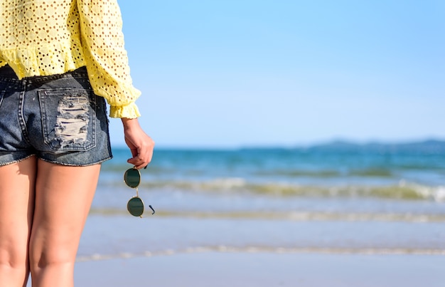 Woman's hand holding sunglasses at blue sea on the beach