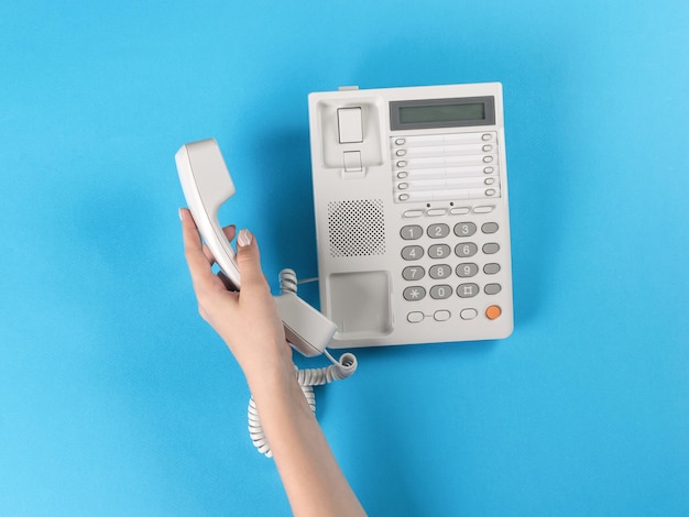 A woman's hand holding a telephone receiver near a telephone on a blue background