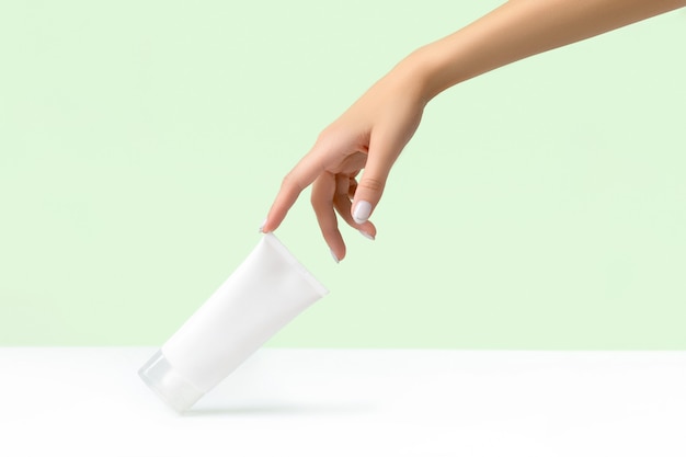 Woman's hand holding white tube on pastel green