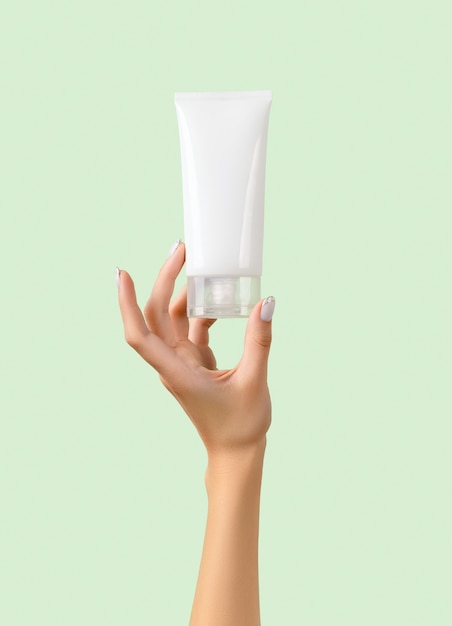 Woman's hand holding white tube on pastel green