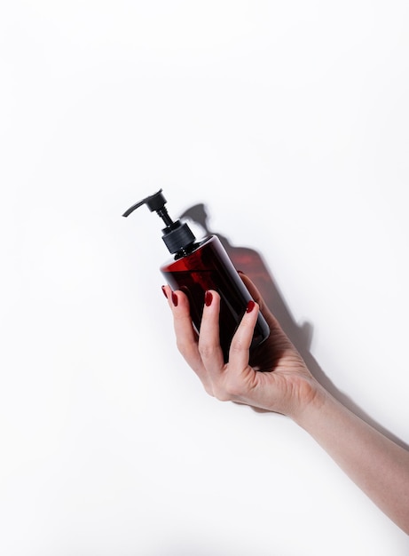 A woman's hand holds a bottle of cosmetics with soap sanitizer creme or lotion for face and body on a white background with hard shadow Skin care beauty body treatment concept Copy space