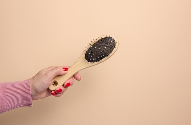 A woman's hand holds a brush for combing animal hair on a beige background