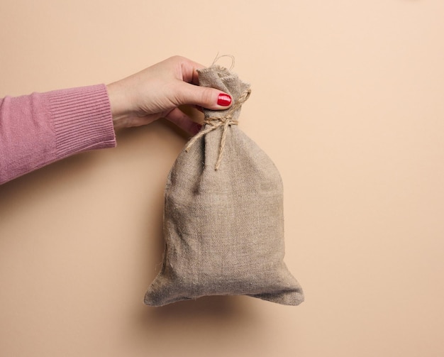 A woman's hand holds a canvas bag on a beige background the concept of a subsidy help