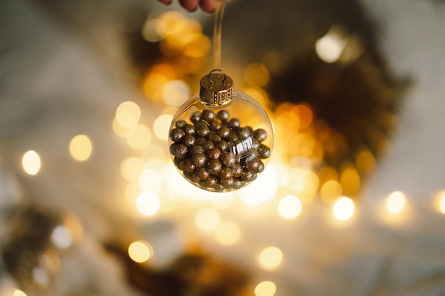 A woman's hand holds a Christmas golden ball on a festive background with golden lights Christmas mood and atmospheric winter time Happy New Year celebration concept