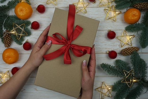 A woman's hand holds a gift in a craft package with a red satin bow