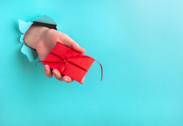 A woman's hand holds a gift through a hole on a turquoise background