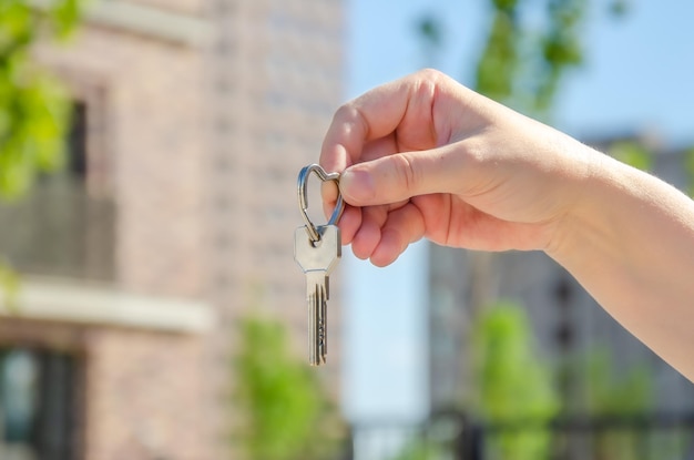 Photo woman's hand holds keys against a blurry background of new buildings