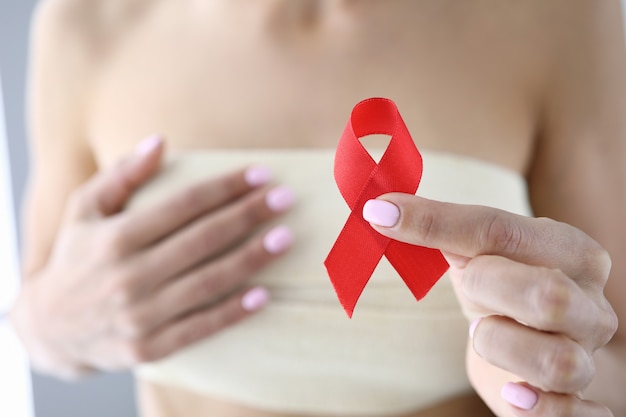 Woman's hand holds red ribbon in her hand and holds other hand on her chest in bandage.