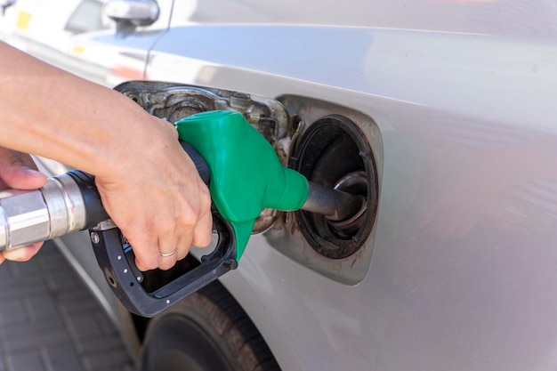 A woman's hand holds a refueling gun in the neck of the tank of the car