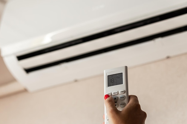 A woman's hand holds a remote control to turn on the air conditioner