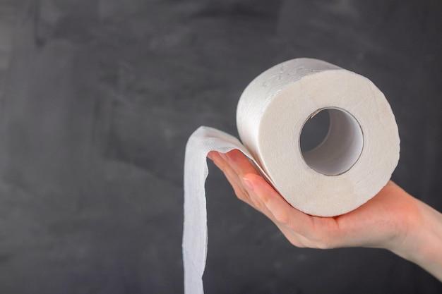 A woman's hand holds a roll of toilet paper on a gray background