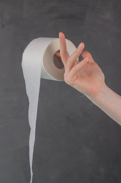 A woman's hand holds a roll of toilet paper on a gray background