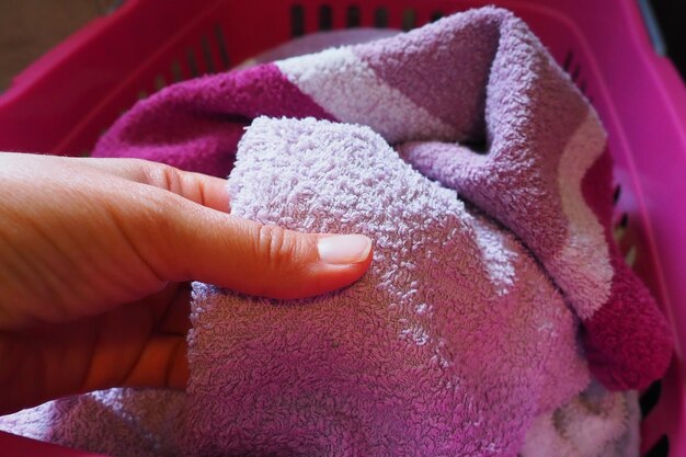 A woman's hand is feeling a cotton colored towel from a basket with dirty laundry Laundry sorting and washing Laundry room or bathroom Housekeeping Pink and blue terry towels