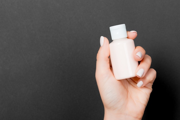 Woman's hand is holding a cosmetics bottle at black background with copy space for your design.