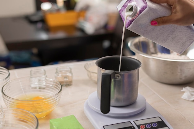 Woman's hand pouring milk into a container to weigh on a scale and make bread