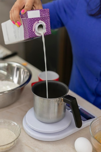 Woman's hand pouring milk into a container to weigh on a scale and make bread