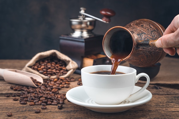 A woman's hand pours coffee into a mug of Turki on the wall of a coffee grinder and coffee beans. Side view, copy space. Tinted image.