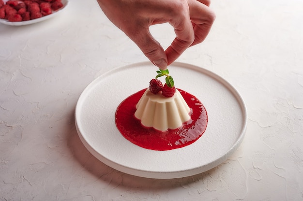 Woman's hand puts mint leaf to panna cotta with syrup and berries