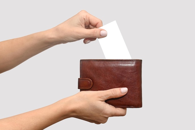 A woman's hand puts a white business card into a leather purse On a gray background