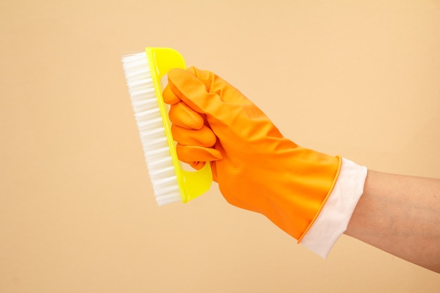 Woman's hand in rubber protective glove with plastic brush on beige background. Washing and cleaning concept.