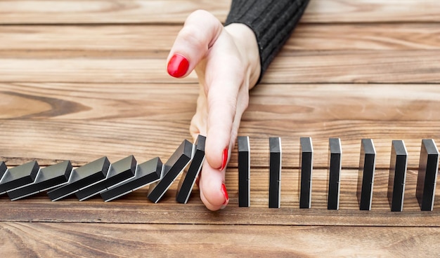 Woman's hand stopping domino effect on the desk Close up