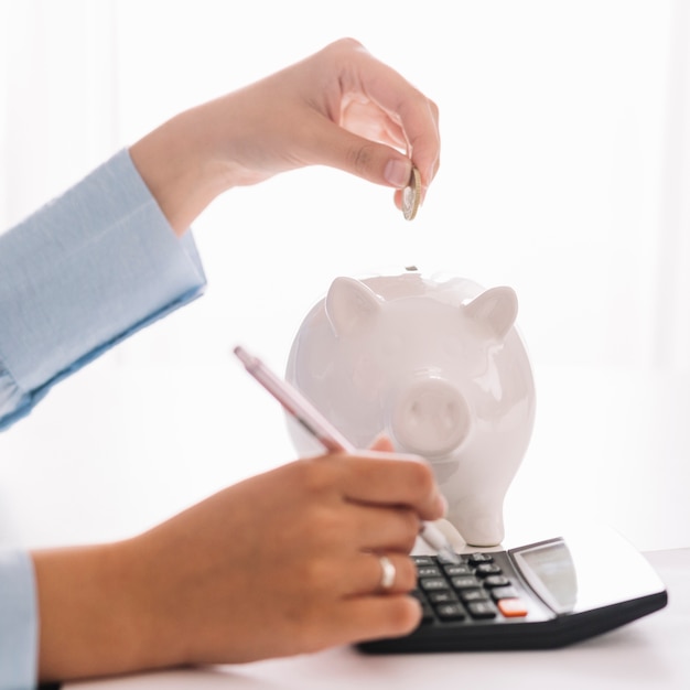 Woman's hand using calculator while inserting coin in piggybank