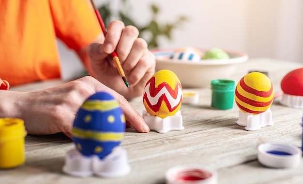 Woman's hand with a brush is drawing a colored pattern on an Easter egg Preparation for the bright Easter holiday