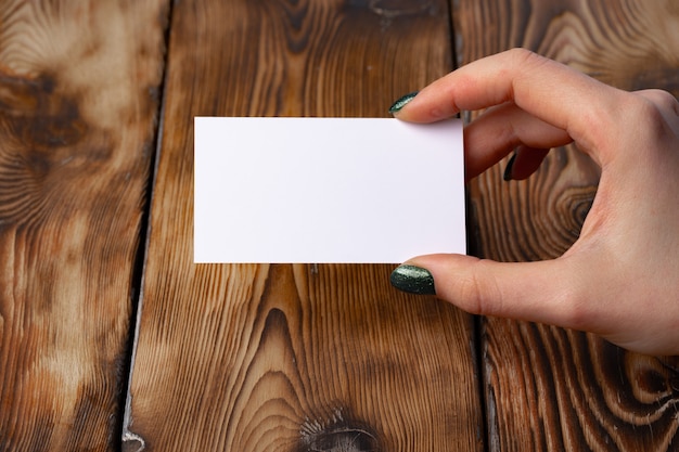 Woman's hand with manicure holding white business card above the table