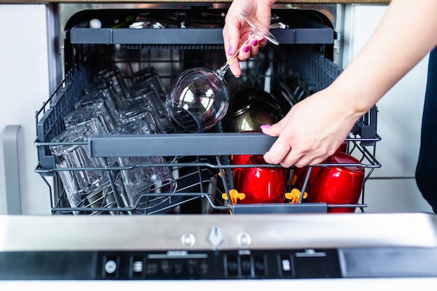 Woman's hand with an open dishwasher filled with clean dishes.