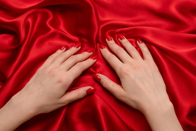 A woman's hand with red nails is trying to rip off a red silk fabric