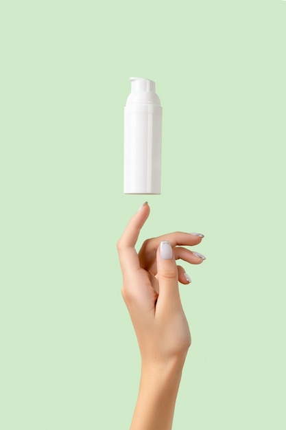 Woman's hand with a white bottle on pastel green