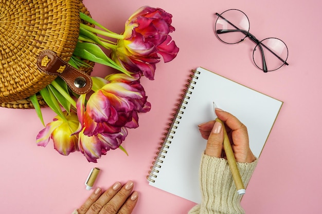 A woman's hand writes down plans in a notebook there are tulips in a wicker bag on the table