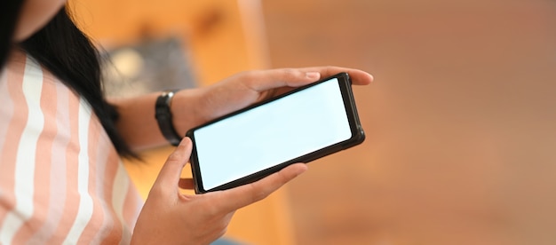 A woman's hands are holding a white blank screen smartphone in the comfortable living room.