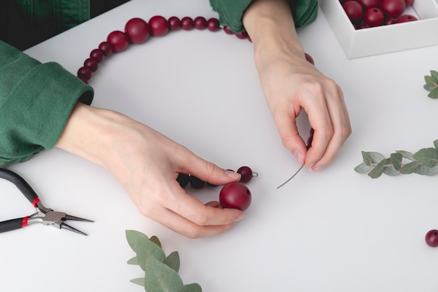 Woman's hands are stringing red colored beads on a wire