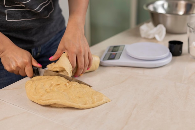 Woman's hands cutting dough to make bread to weigh on a scale