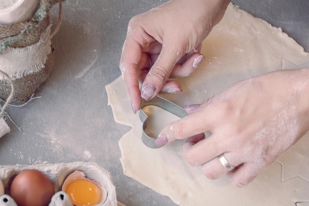 Woman's hands cutting the dough with a baking tin in a heart shape