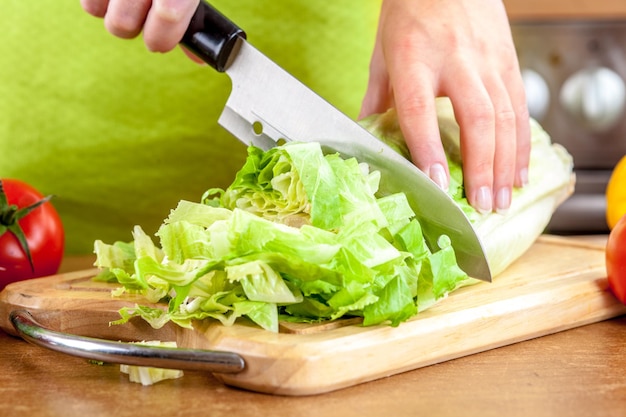 Photo woman's hands cutting lettuce, behind fresh vegetables.