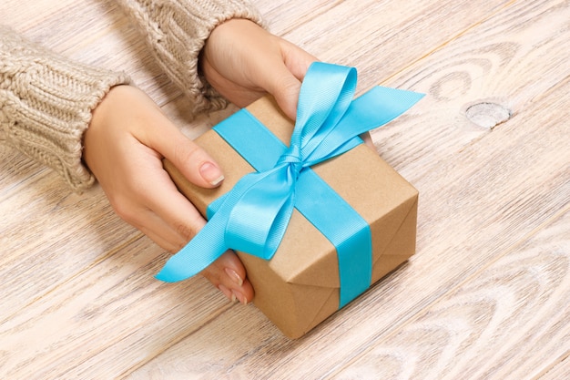 Woman's hands give wrapped valentine holiday handmade present in craft paper with blue ribbon