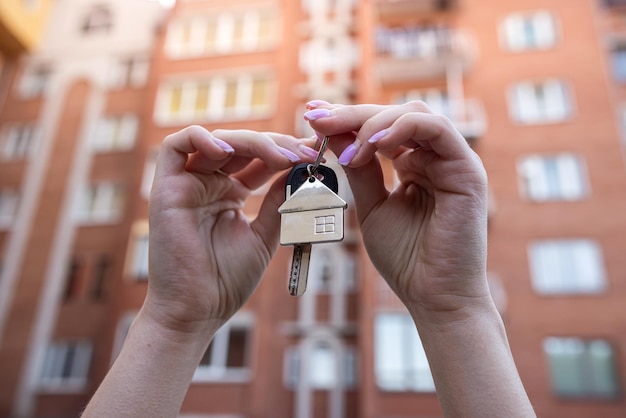 Woman's hands hold the keys on the background of new building from newly purchased apartment