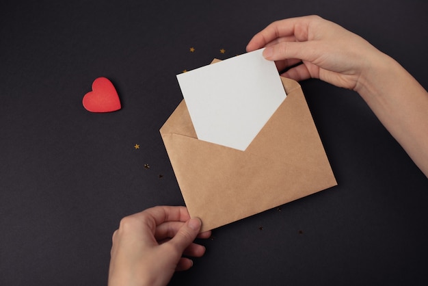 Woman's hands holding an envelope with a blank sheet of paper inside. Dark (black) background.