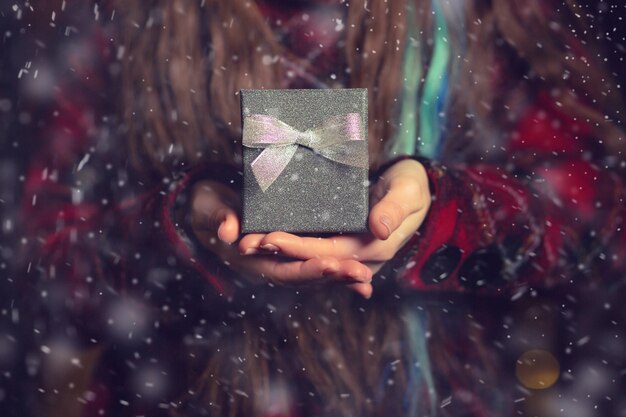 Woman's hands holding a gift box with a bow at the street during the snowfall